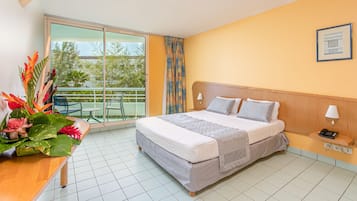 Habitación de hotel con cama, mesita de noche, lámpara, teléfono y vistas al exterior a través de una puerta corredera.