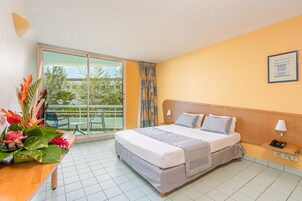 Habitación de hotel con cama, mesita de noche, lámpara, teléfono y vistas al exterior a través de una puerta corredera.