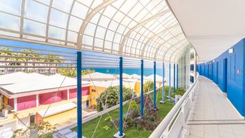 A covered outdoor area with a glass ceiling, blue railings, and a view of buildings and greenery below.