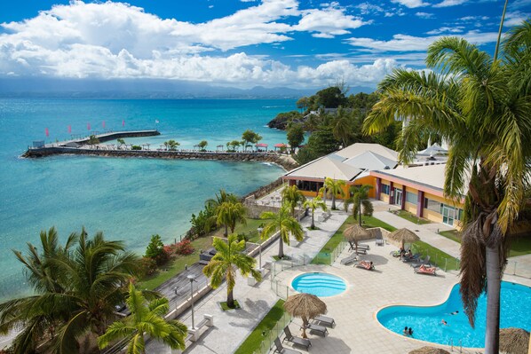 A resort with a swimming pool, lounge chairs, and a pier extending into the sea.