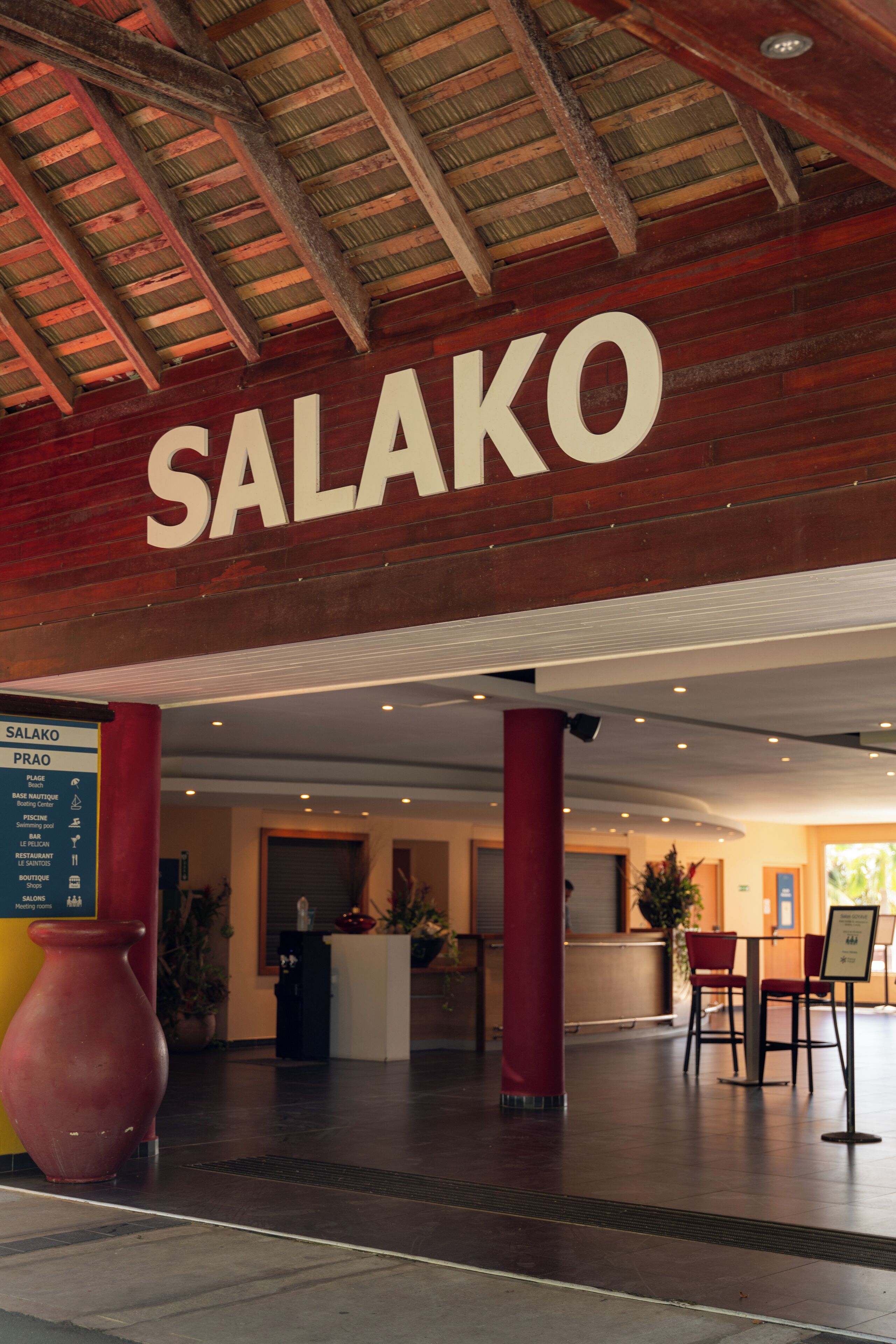 Een hotel lobby met een opvallend 'SALAKO' bord, een receptiebalie en rode zuilen.