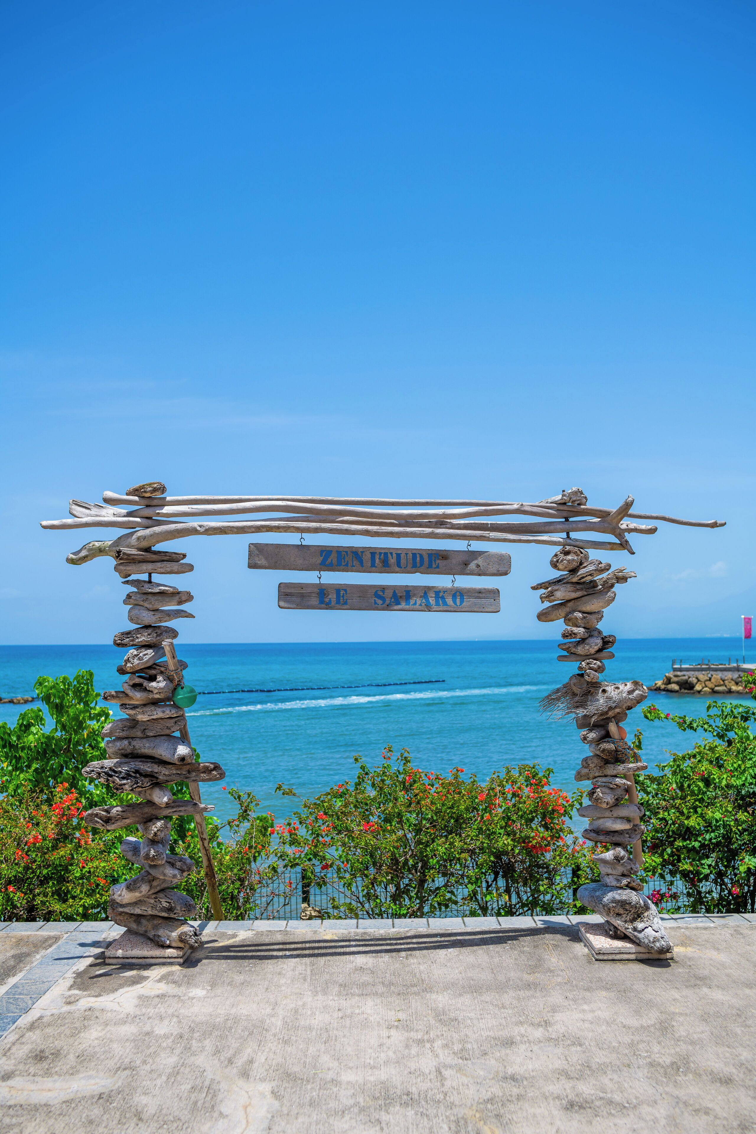 A wooden structure with a sign reading "ZENITURE RE SALAKO" against a backdrop of a clear blue sky and ocean.