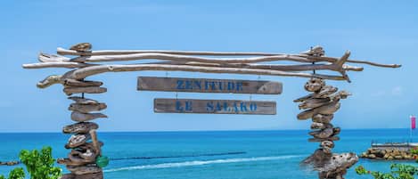 A wooden structure with a sign reading "ZENITURE RE SALAKO" against a backdrop of a clear blue sky and ocean.