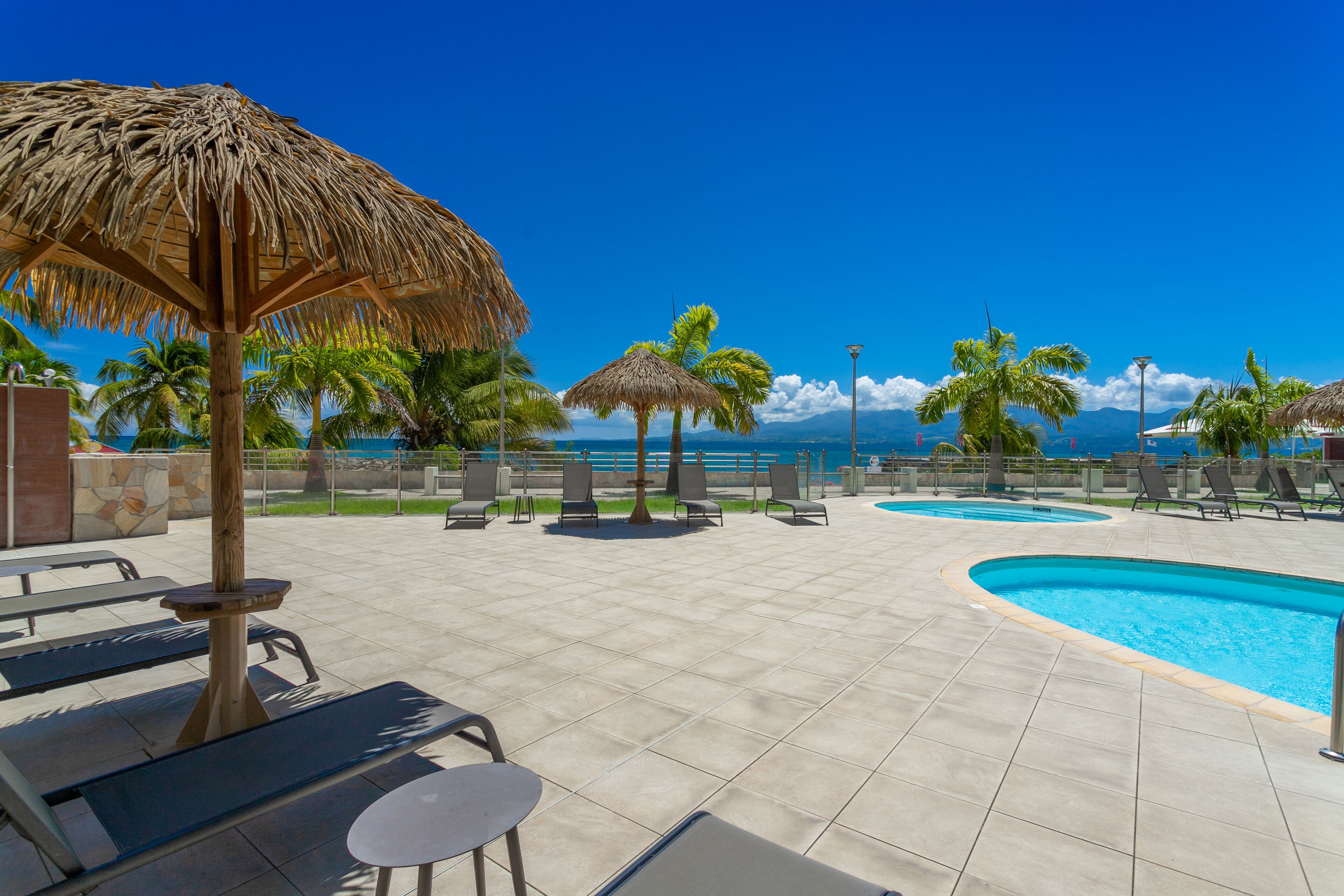 A poolside area with lounge chairs, a thatched umbrella, and a view of the ocean.