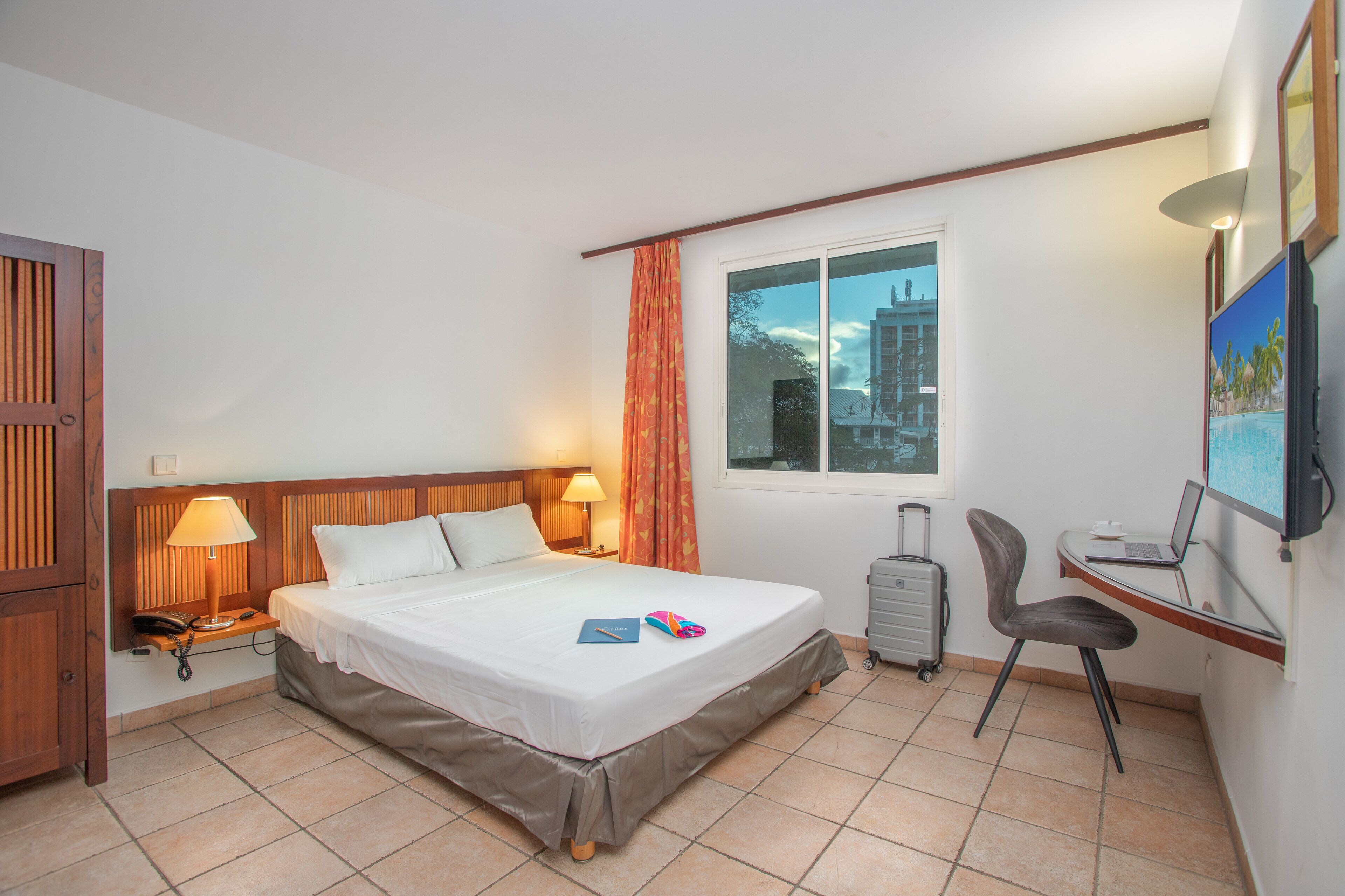 A hotel room with a bed, desk, chair, and a window with a view of buildings.