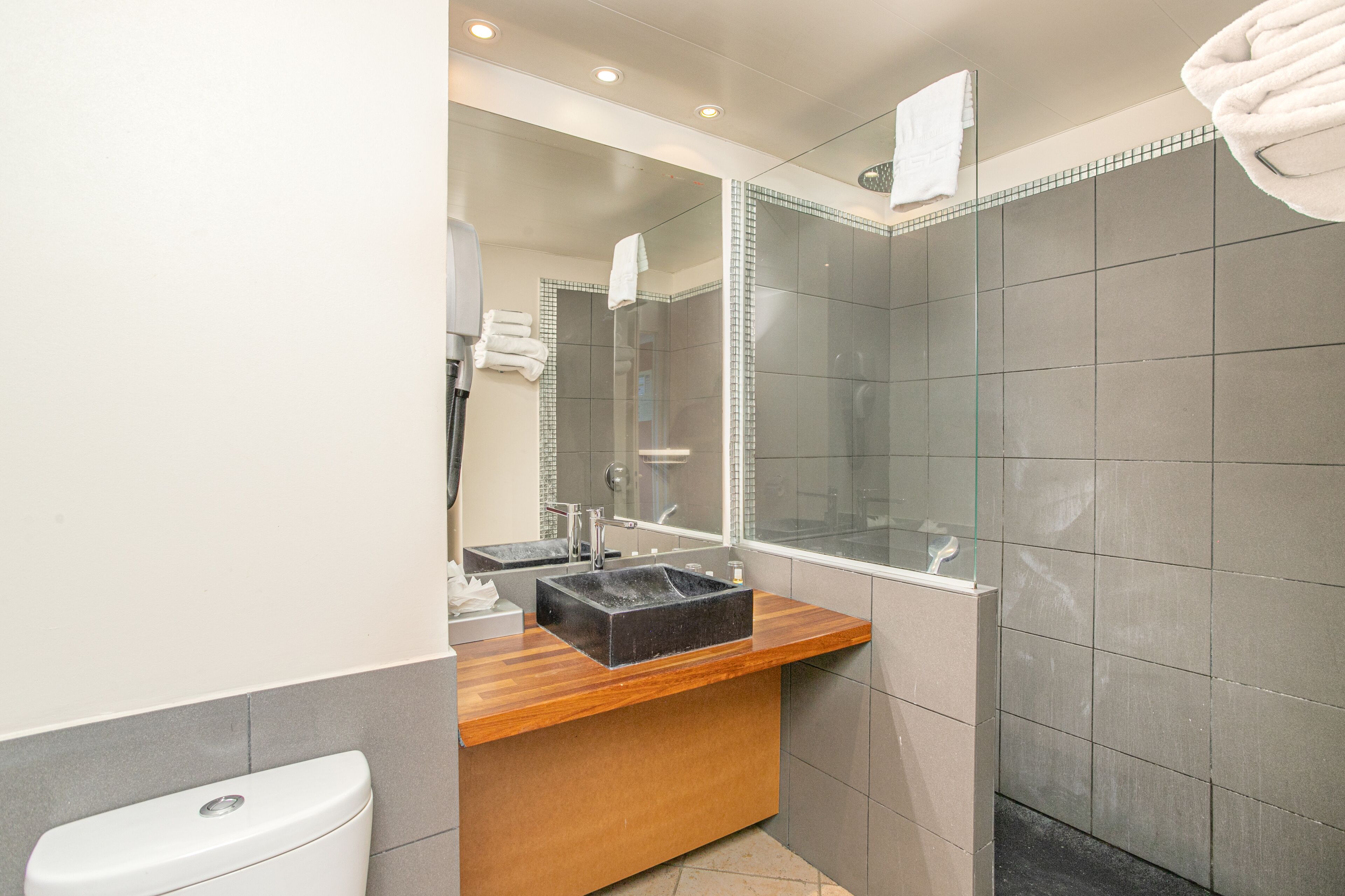 A modern bathroom with a wooden vanity, a glass shower enclosure, and a large mirror.