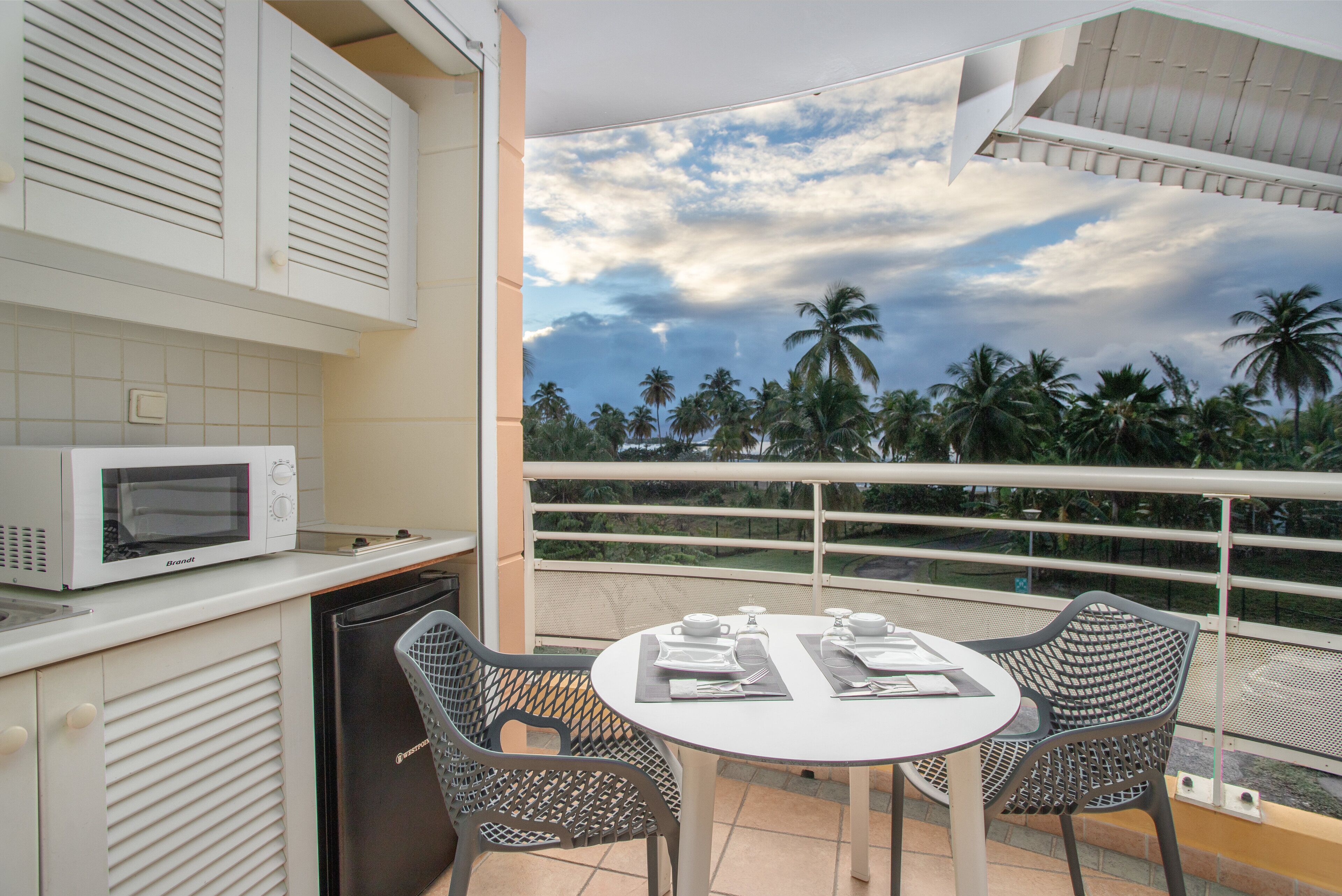 A balcony with a white table and chairs, a microwave, and a dishwasher.