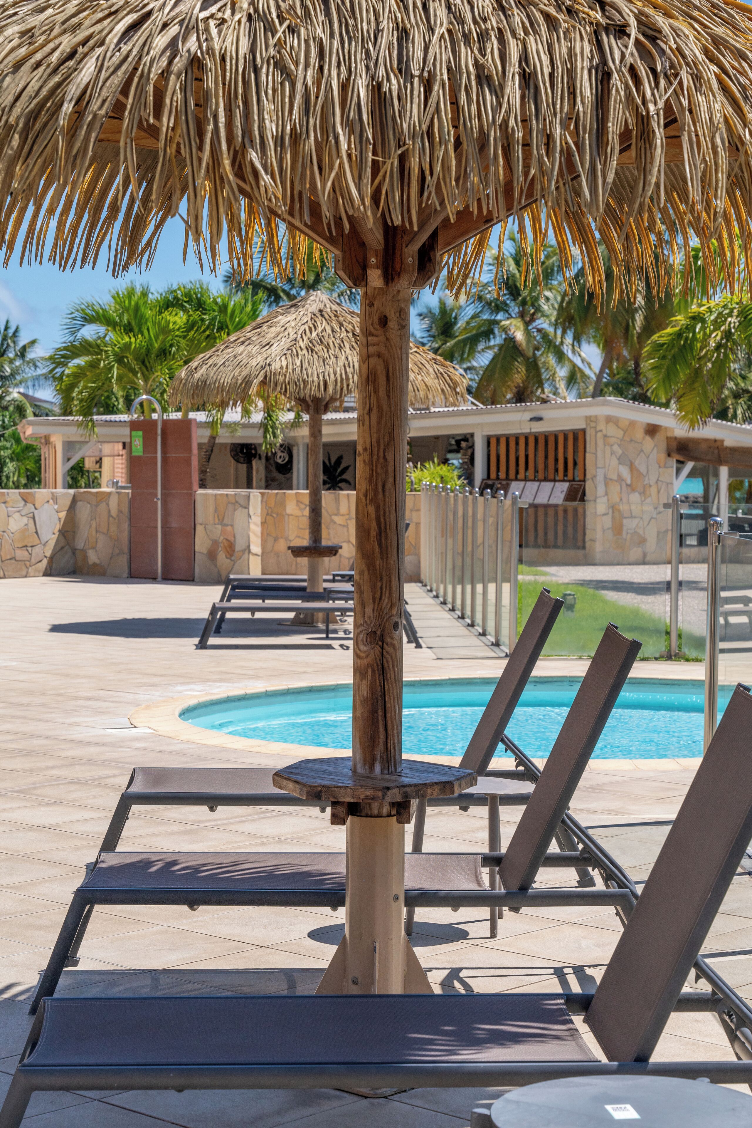 A poolside area with lounge chairs, a thatched umbrella, and a stone building in the background.