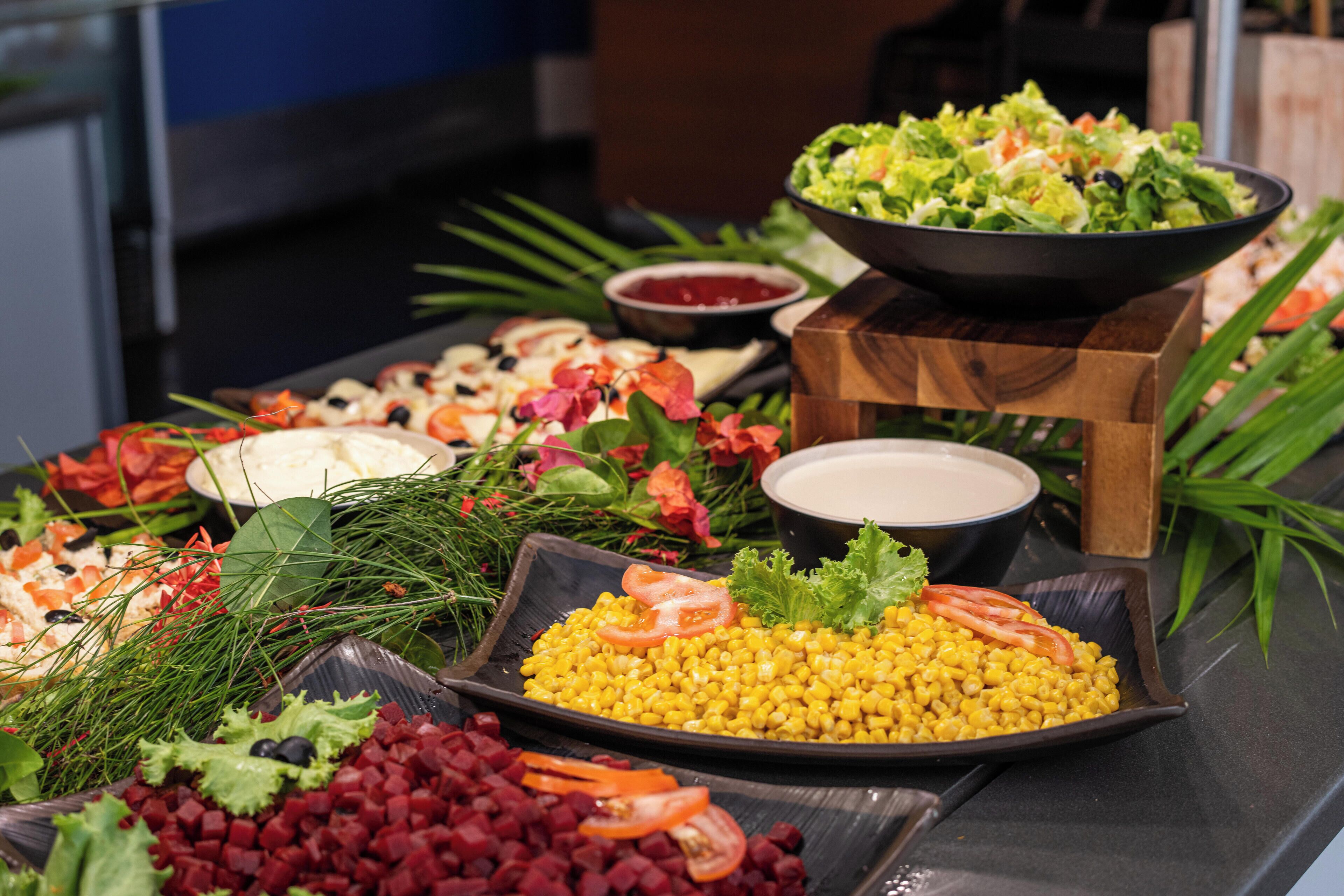 A buffet table with various dishes including corn, salad, and other food items.