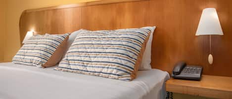 A hotel room with a wooden headboard, two striped pillows, a bedside lamp, and a telephone on a wooden nightstand.