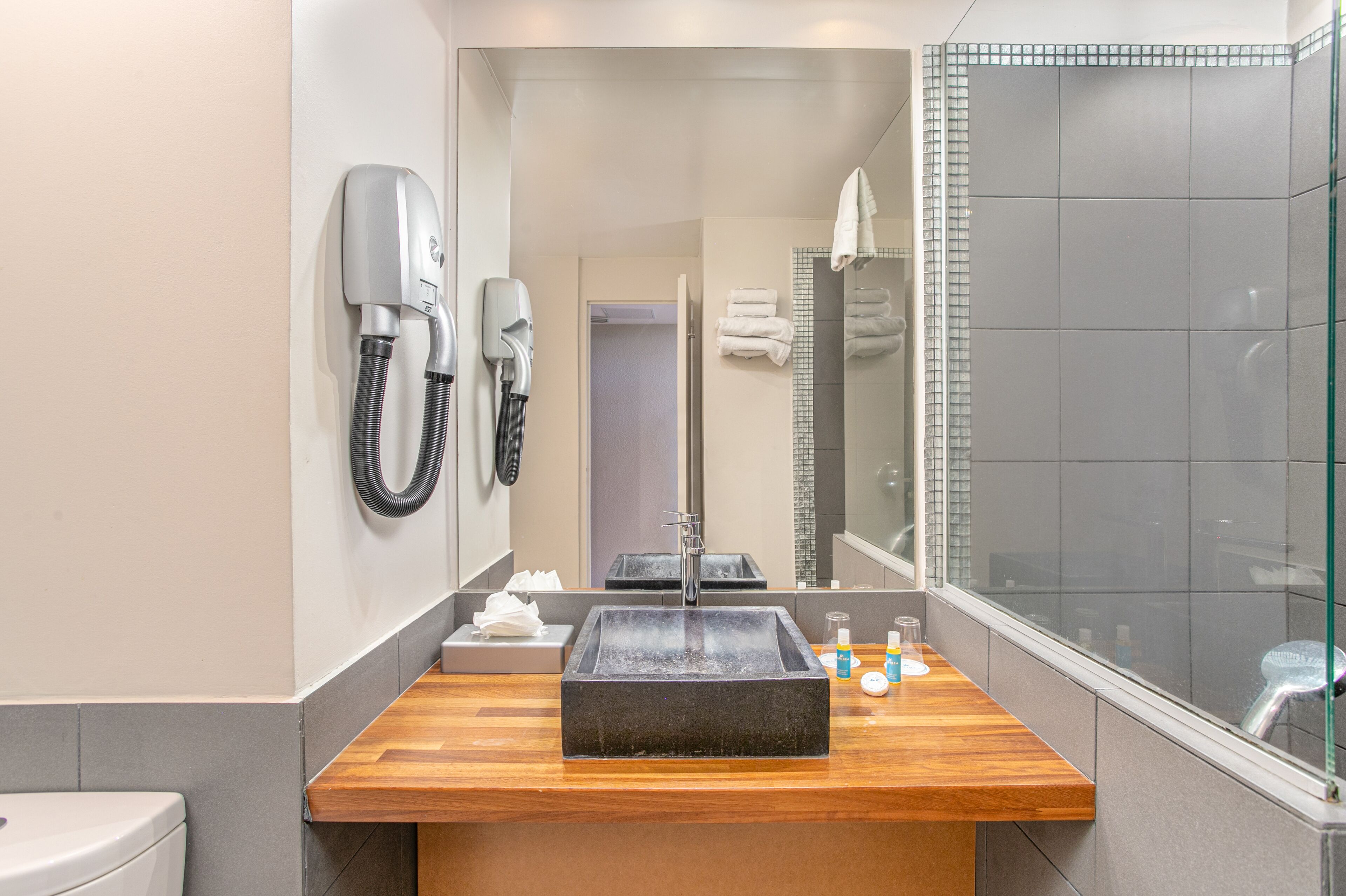 Un baño moderno con tocador de madera, un espejo grande, cabina de ducha de vidrio y un secador de pelo montado en la pared.