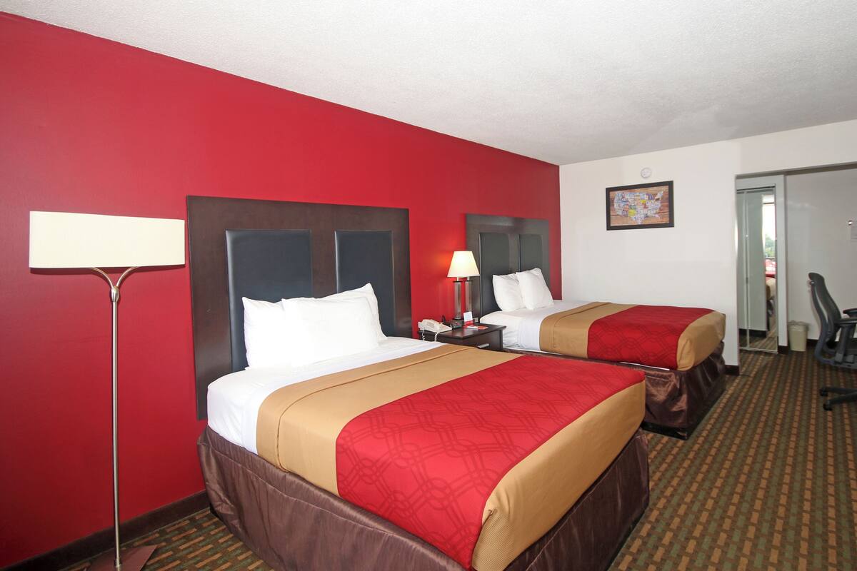 Quarto de hotel com duas camas, uma escrivaninha, uma cadeira, um abajur e um mapa na parede.