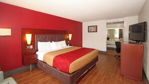 A hotel room with a large bed, wooden flooring, a red accent wall, a desk with a chair, and a television. - Americas Best Value Inn Pilot Mountain (Pilot Mountain)