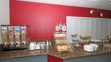 A kitchen area with a red wall, a white door, and a clock. There are cereal boxes, a coffee maker, and a display case with pastries.