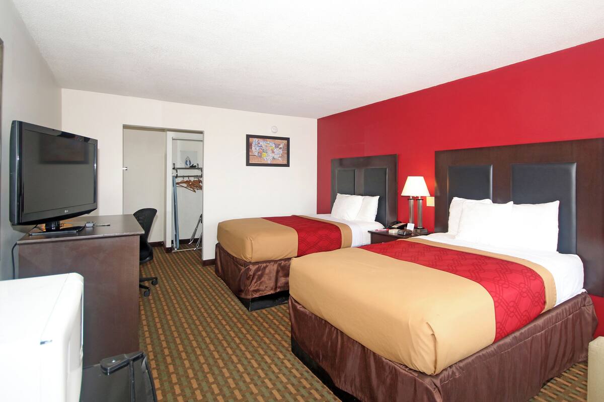 Quarto de hotel com duas camas, televisão, escrivaninha e guarda-roupa.