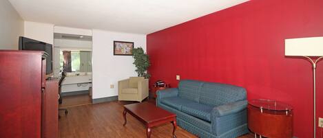 A living room with a red wall, a blue sofa, a wooden coffee table, a red cabinet, and a television.