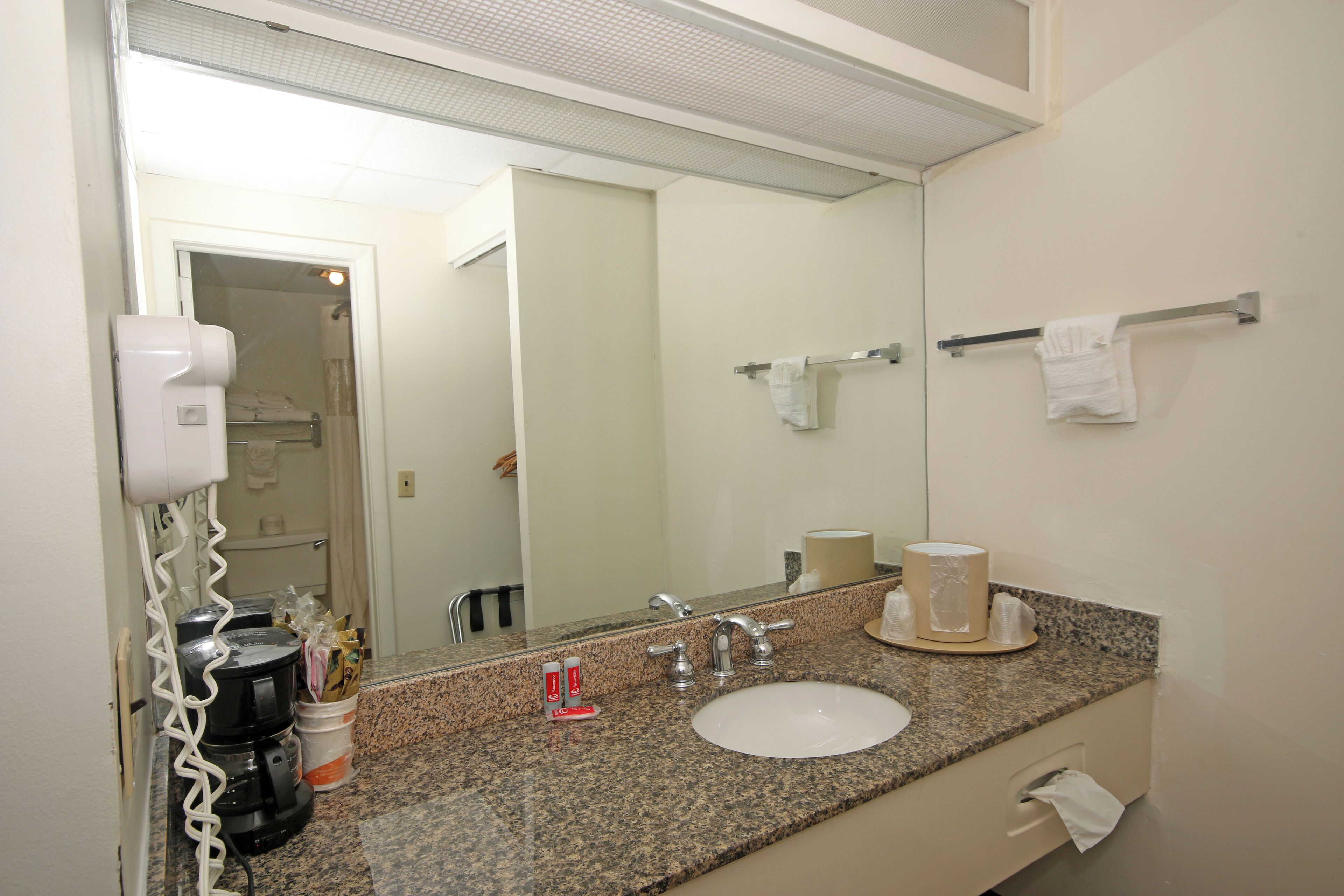 Un baño con encimera de granito, lavabo blanco, espejo, toallero y secador de pelo.