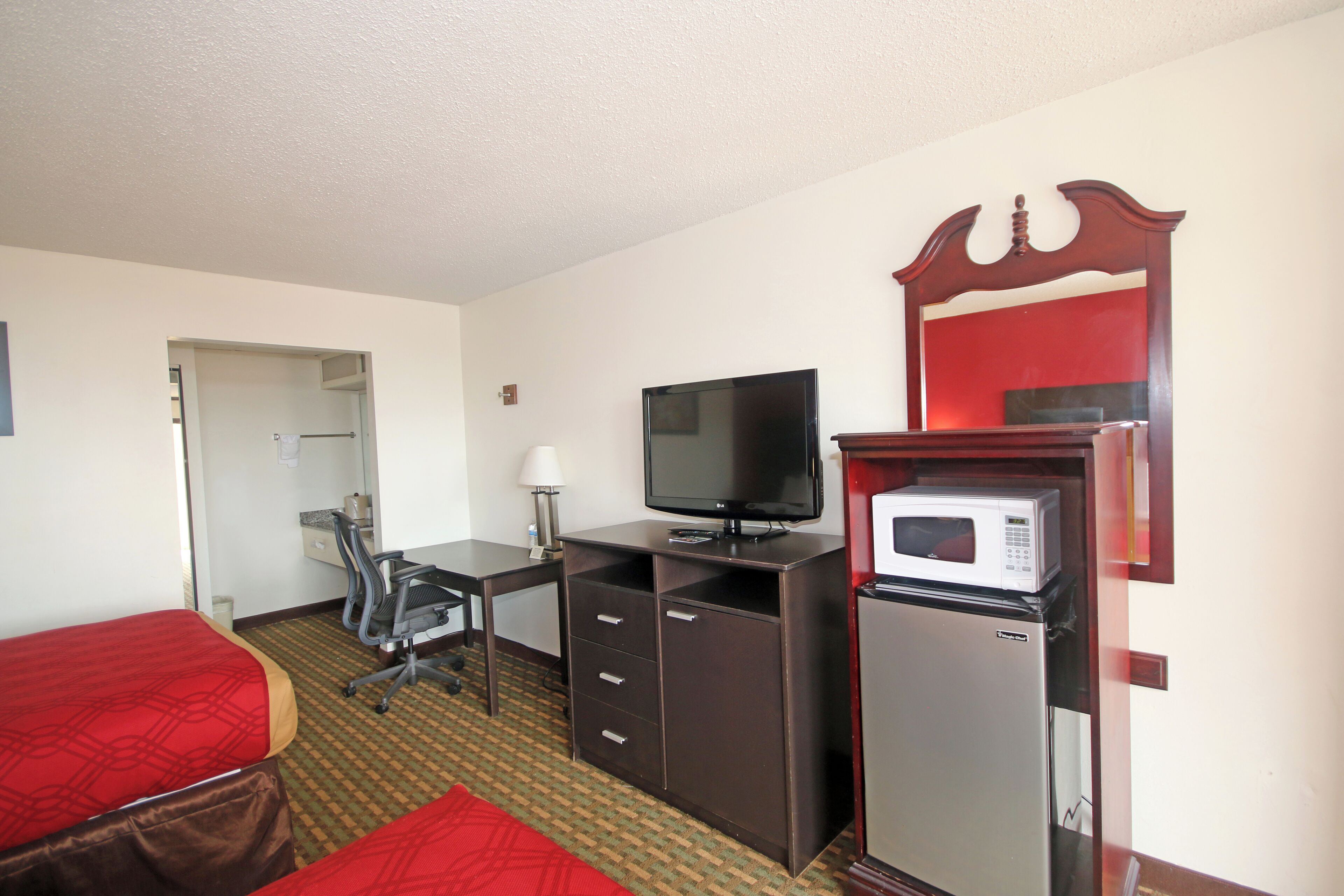 A hotel room with two single beds, a desk with a television, a microwave, and a refrigerator.