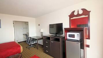 A hotel room with two single beds, a desk with a television, a microwave, and a refrigerator.