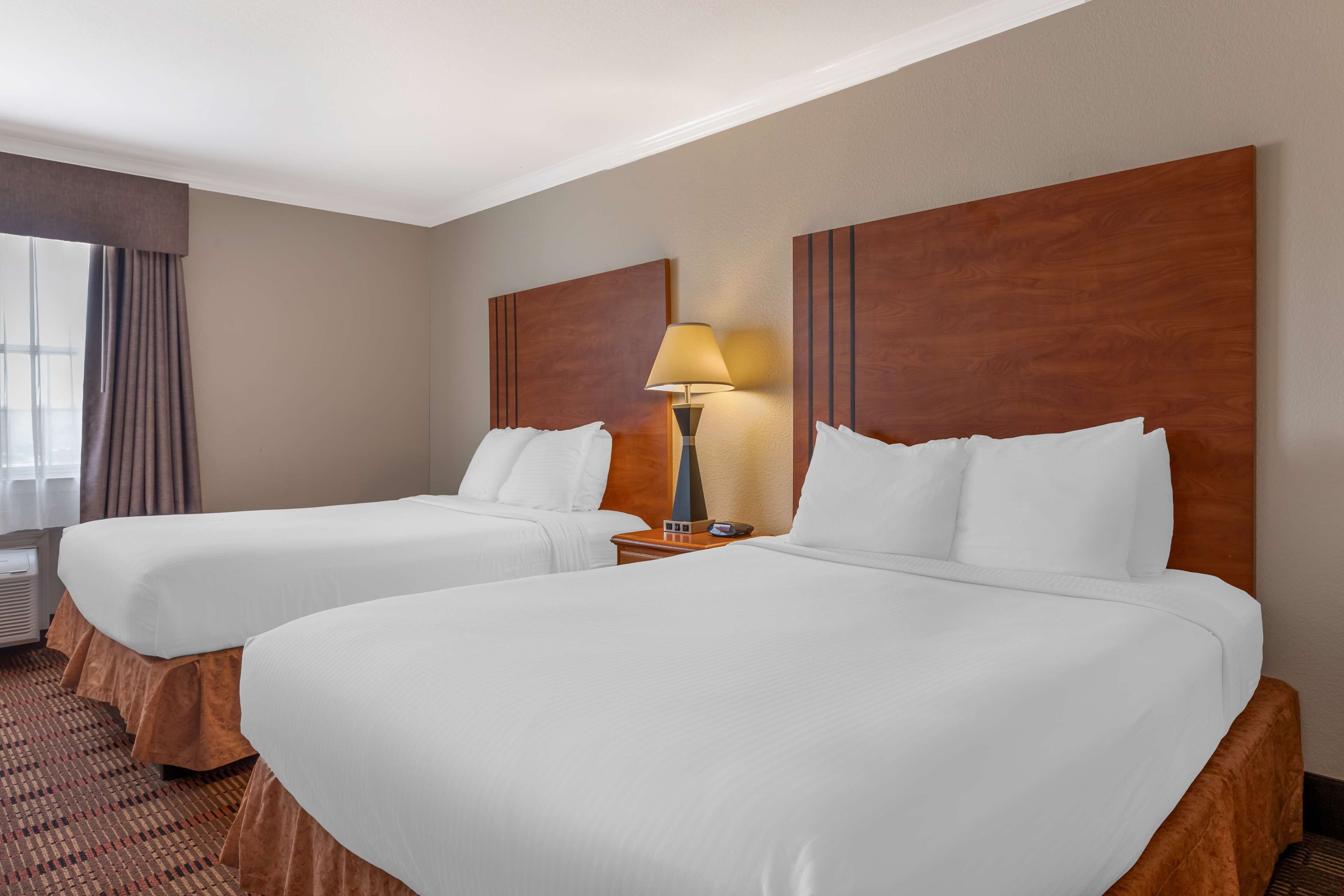 A hotel room with two beds, a nightstand with a lamp, and a window with curtains.