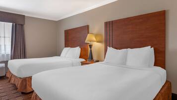 A hotel room with two beds, a nightstand with a lamp, and a window with curtains.