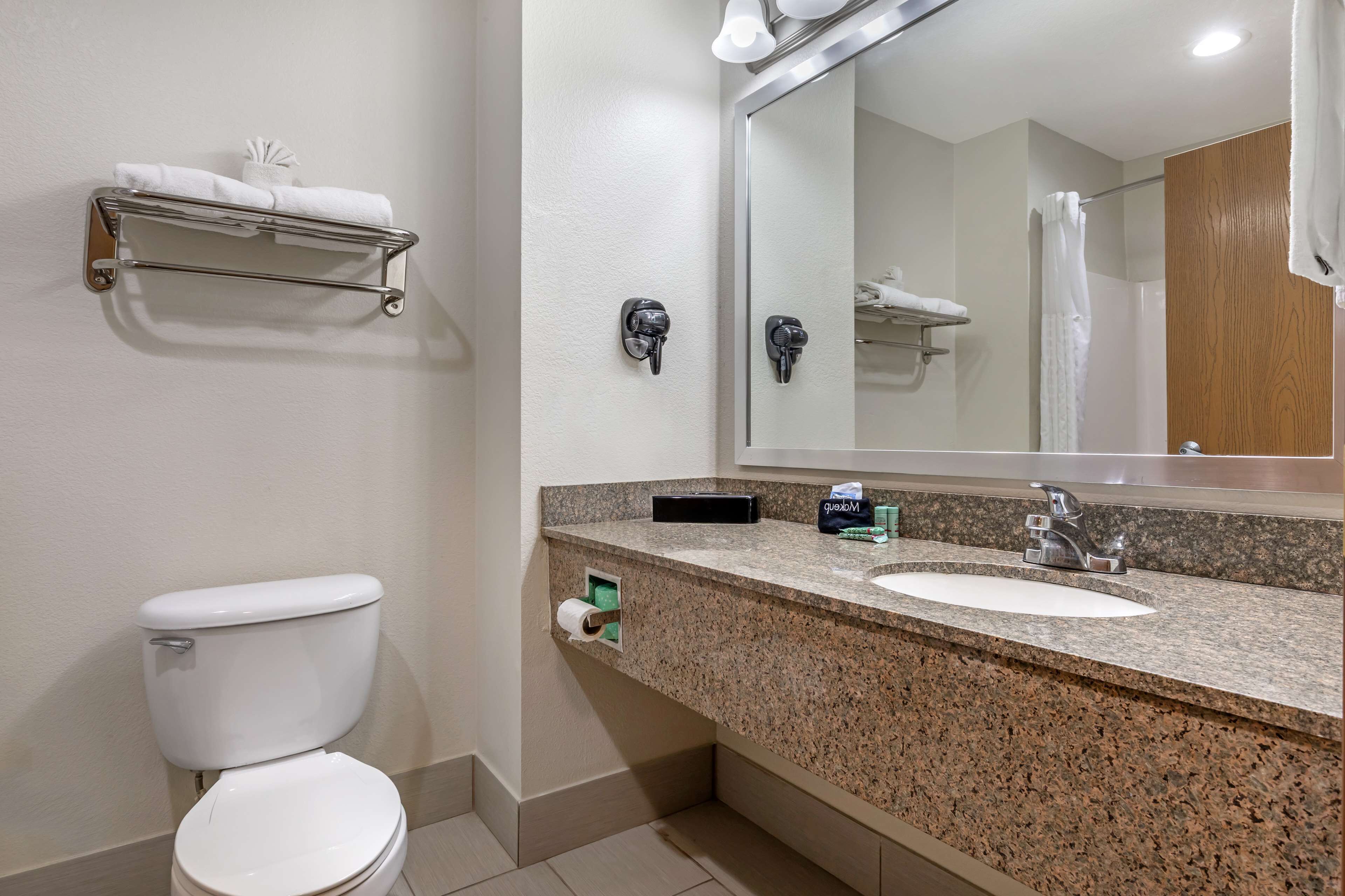 A bathroom with a toilet, sink, mirror, towel rack, and a small shelf with toiletries.