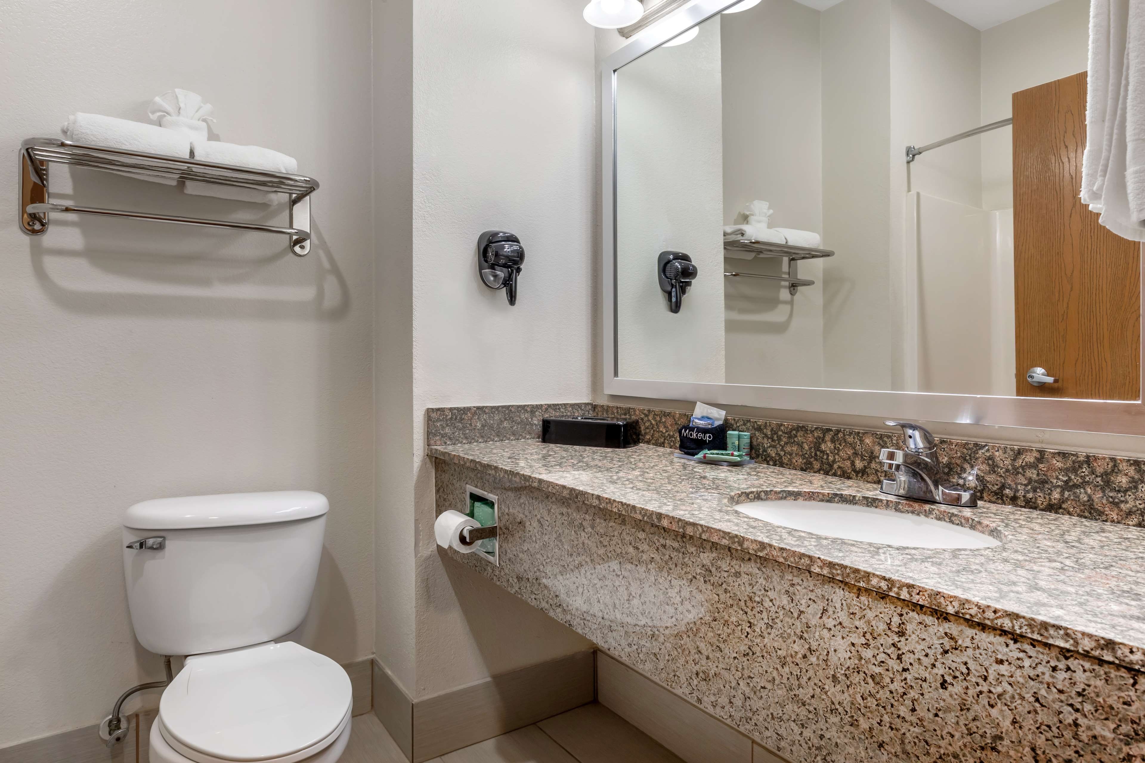 A bathroom with a toilet, sink, mirror, towel rack, and a makeup station.