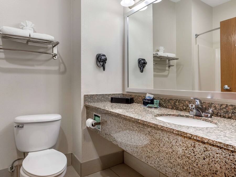 A bathroom with a toilet, sink, mirror, towel rack, and a makeup station.