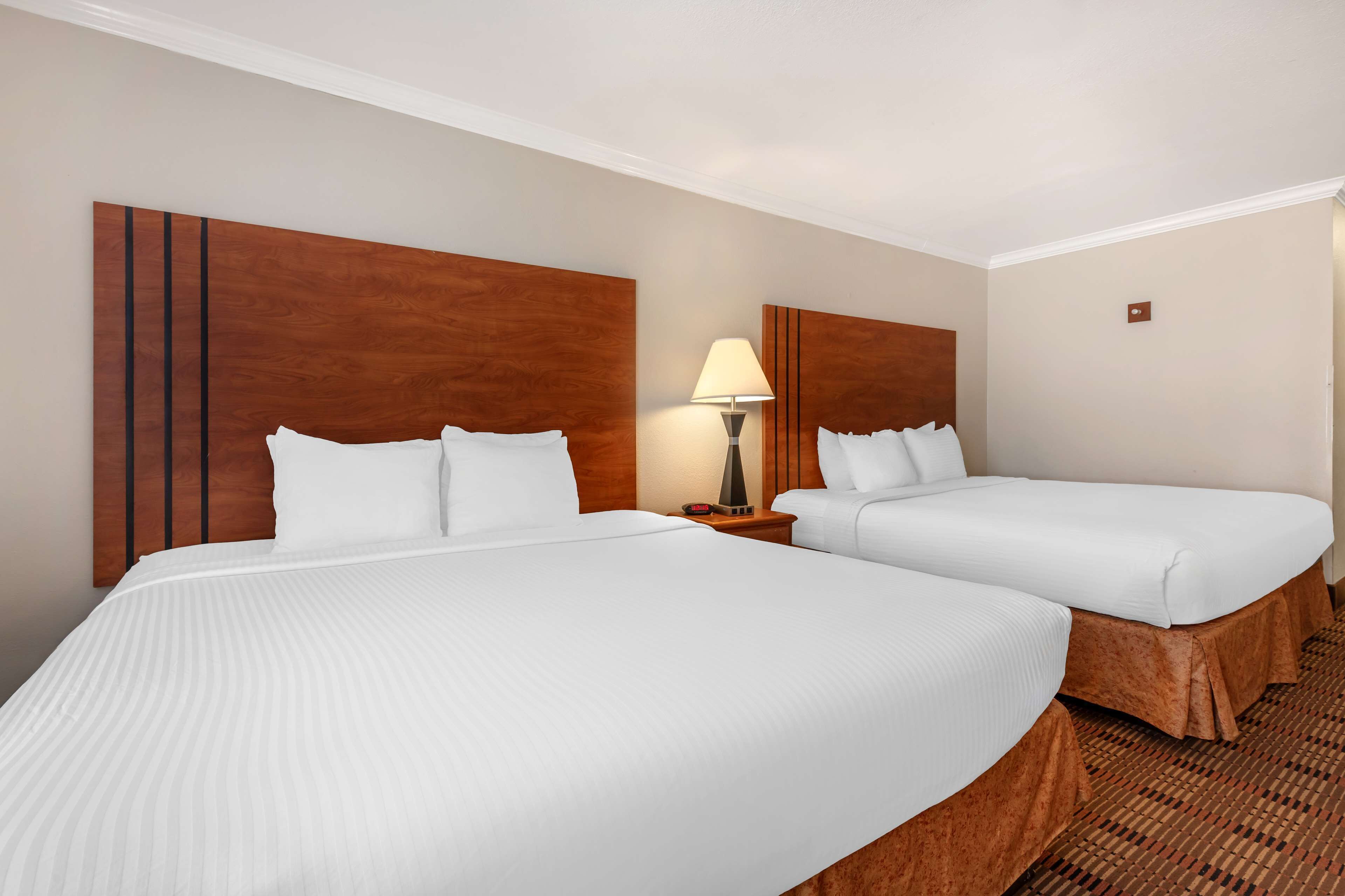 Camera d'albergo con due letti, un comodino con una lampada e una testiera in legno.