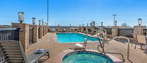 Un espace piscine aménagé sur le toit, avec un jacuzzi, des chaises longues et une vue sur le panorama urbain.