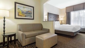 A hotel room with a sofa, ottoman, bed, and a painting on the wall.