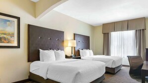 A hotel room with two beds, a desk, a chair, and a painting on the wall.