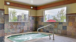 A spa area with a stone wall, a hot tub, and a window with a view of trees and buildings.