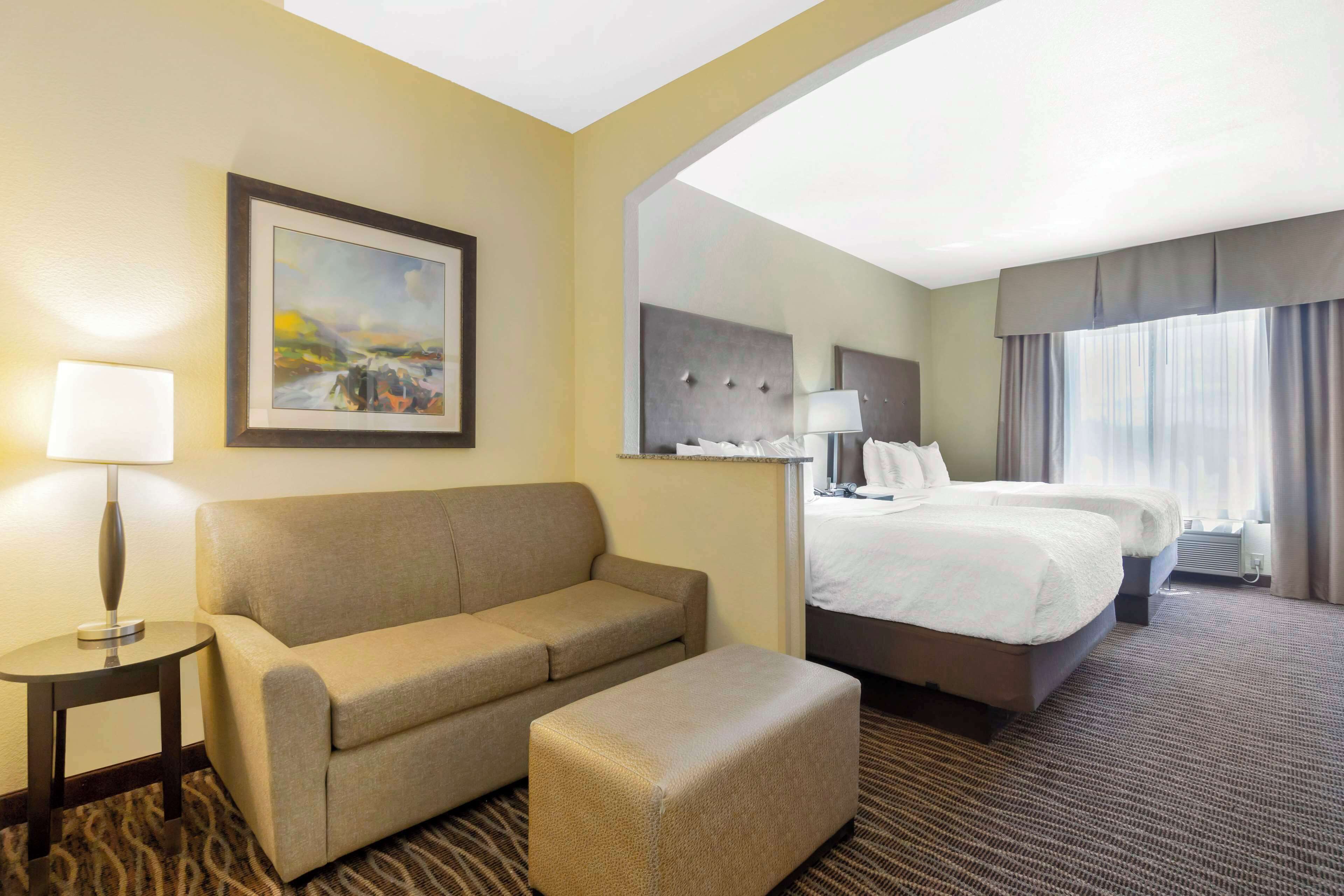 Habitación de hotel con sofá, una mesita de noche con lámpara, cama con cabecero y un espejo grande.