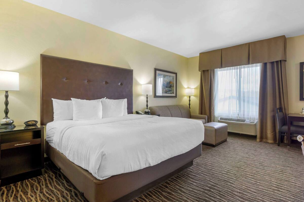 Een hotelkamer met een groot bed, nachtkastjes, een stoel, een bureau en een raam met gordijnen.