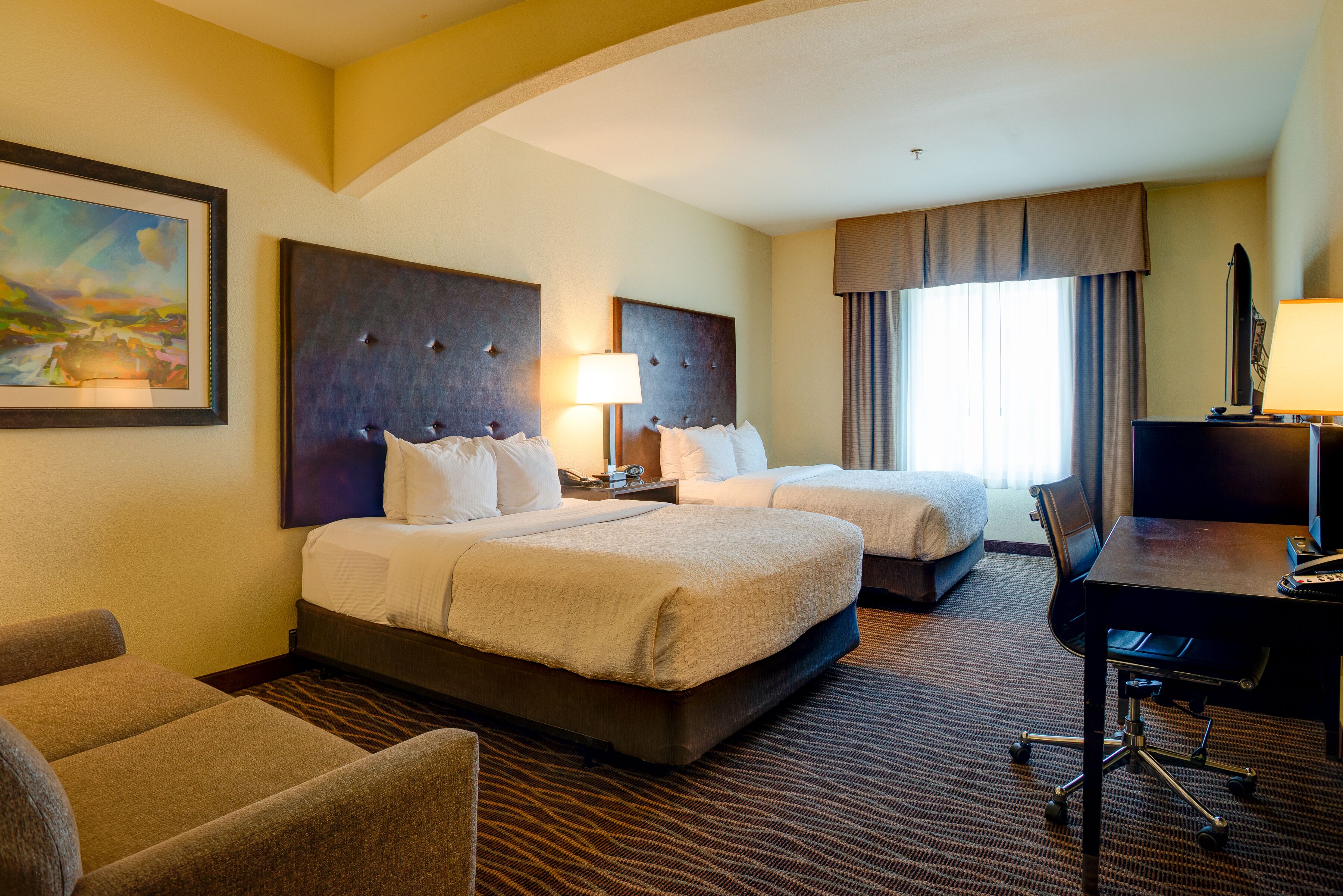 A hotel room with two beds, a desk, and a chair.