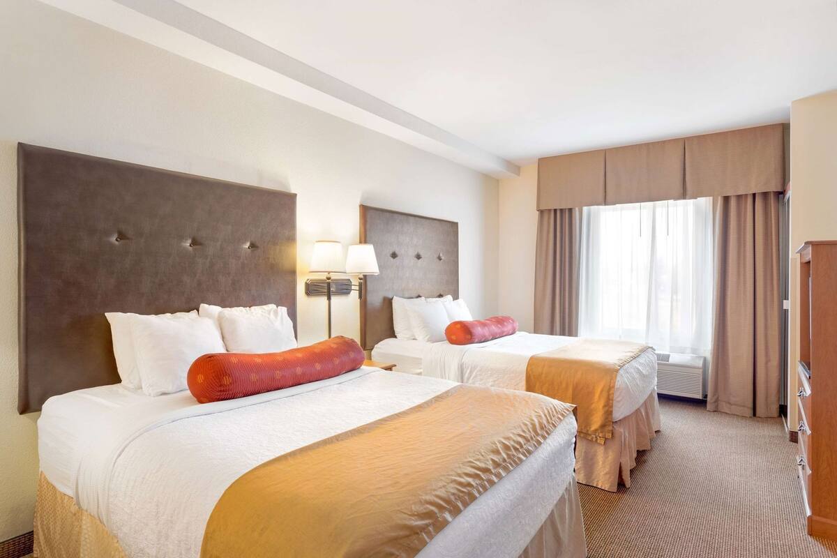Een hotelkamer met twee bedden, een groot raam met gordijnen, een wandlamp en een houten kledingkast.