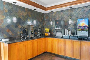A kitchen with wooden cabinets, a coffee machine, a juice dispenser, and a fruit basket.