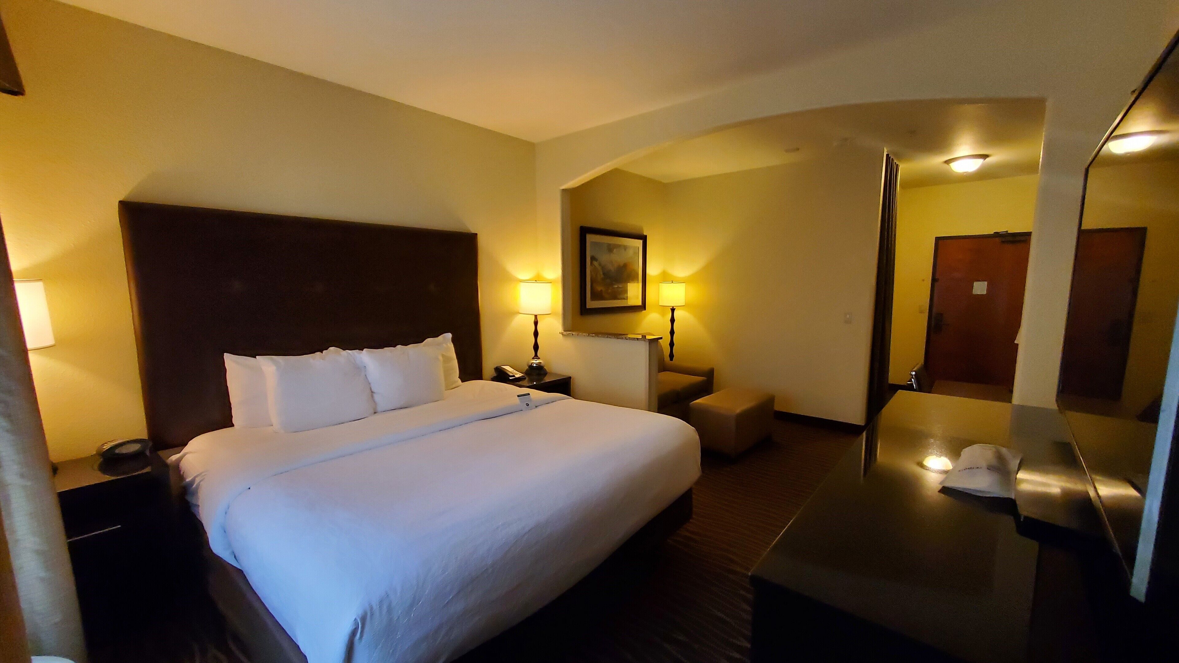 A hotel room with a large bed, a desk, a chair, a mirror, and two bedside lamps.