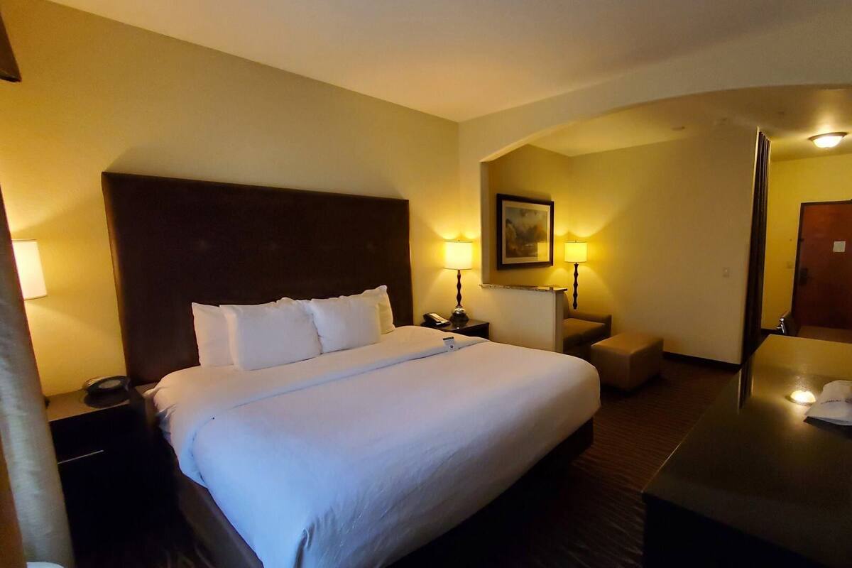 Hotelkamer met een groot bed, nachtkastjes, een bureau, een stoel, een spiegel en een schilderij aan de muur.