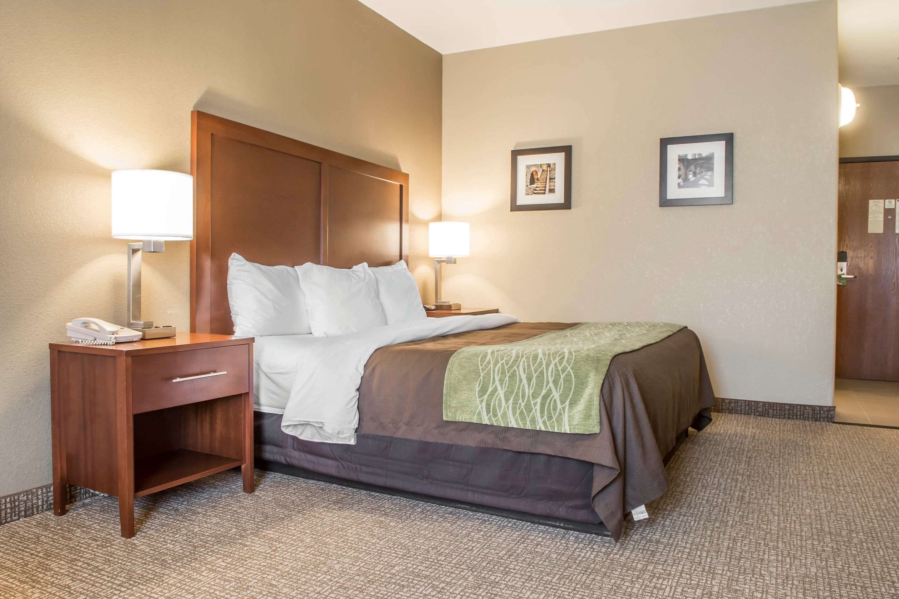 A hotel room with a bed, bedside tables, lamps, a nightstand, and a carpeted floor.