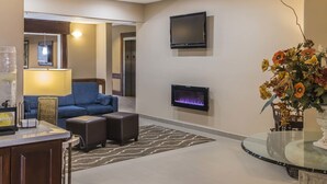 Un hall d’hôtel moderne avec un canapé bleu, une cheminée, un téléviseur et un arrangement floral.