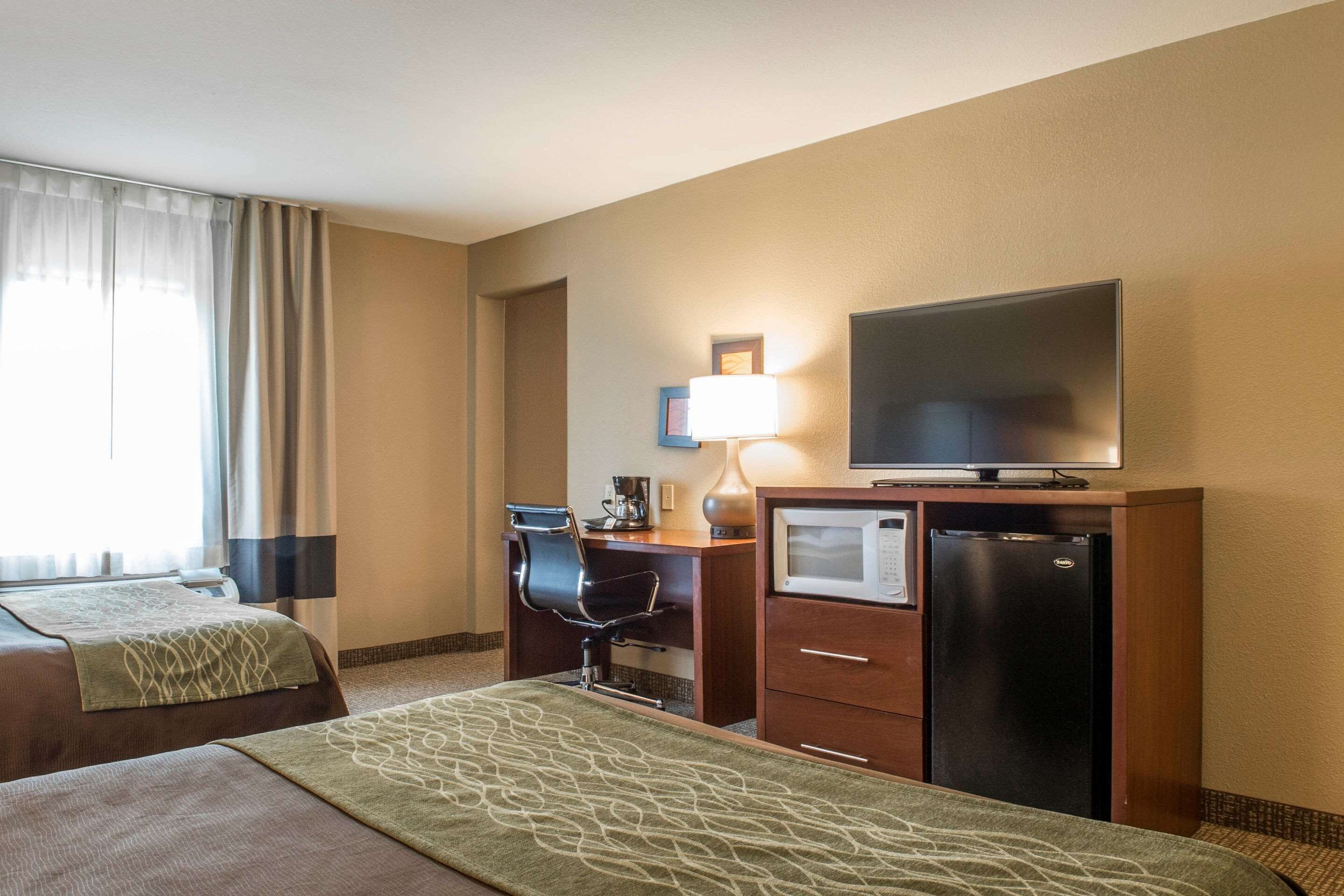 A hotel room with two beds, a desk with a computer, a television, and a refrigerator.
