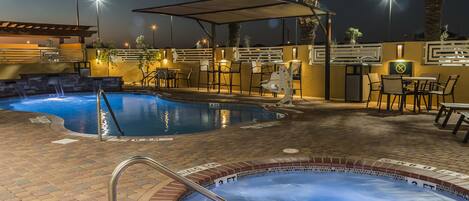 A heated outdoor swimming pool area with lounge chairs and a covered seating area.