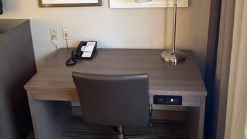 A hotel room with a desk, chair, lamp, phone, and framed pictures on the wall.