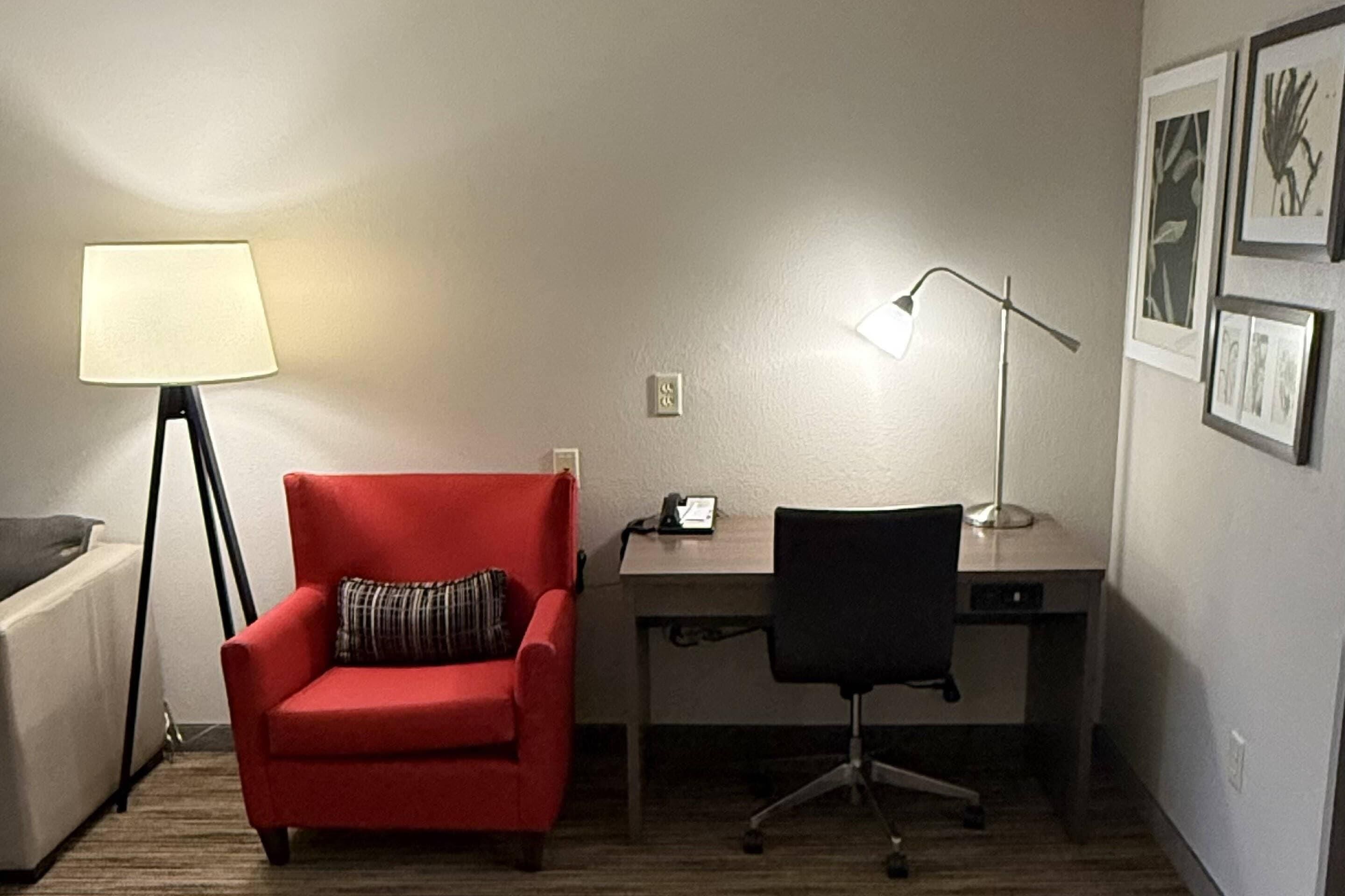 A room with a red armchair, a desk, a lamp, and framed pictures on the wall.