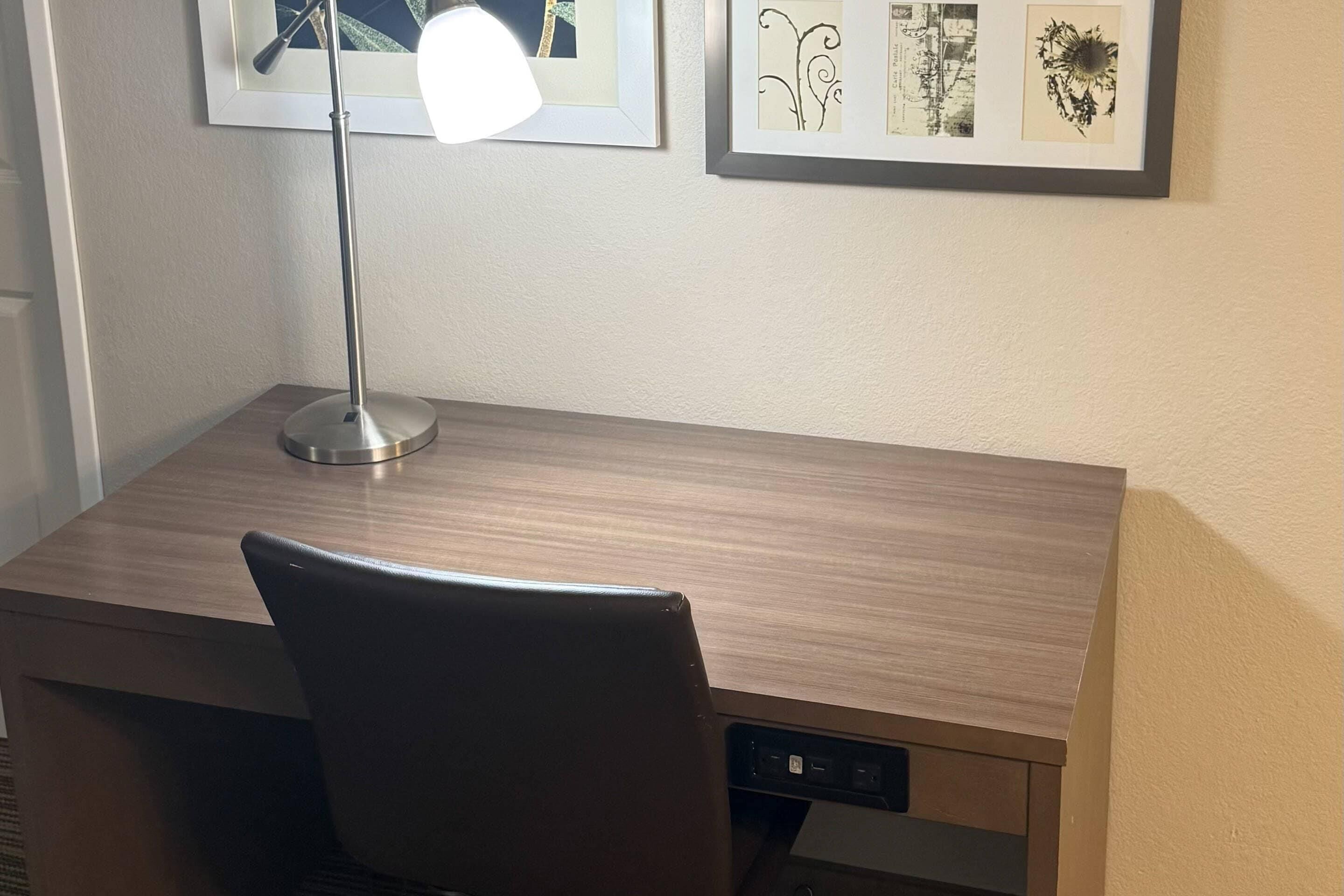 Un escritorio de madera con una lámpara, una silla y cuadros en la pared.