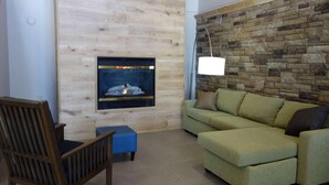 A living room with a wooden wall, a fireplace, a green sofa, a wooden chair, and a floor lamp. - Country Inn & Suites by Radisson, Mason City, IA (Mason City)