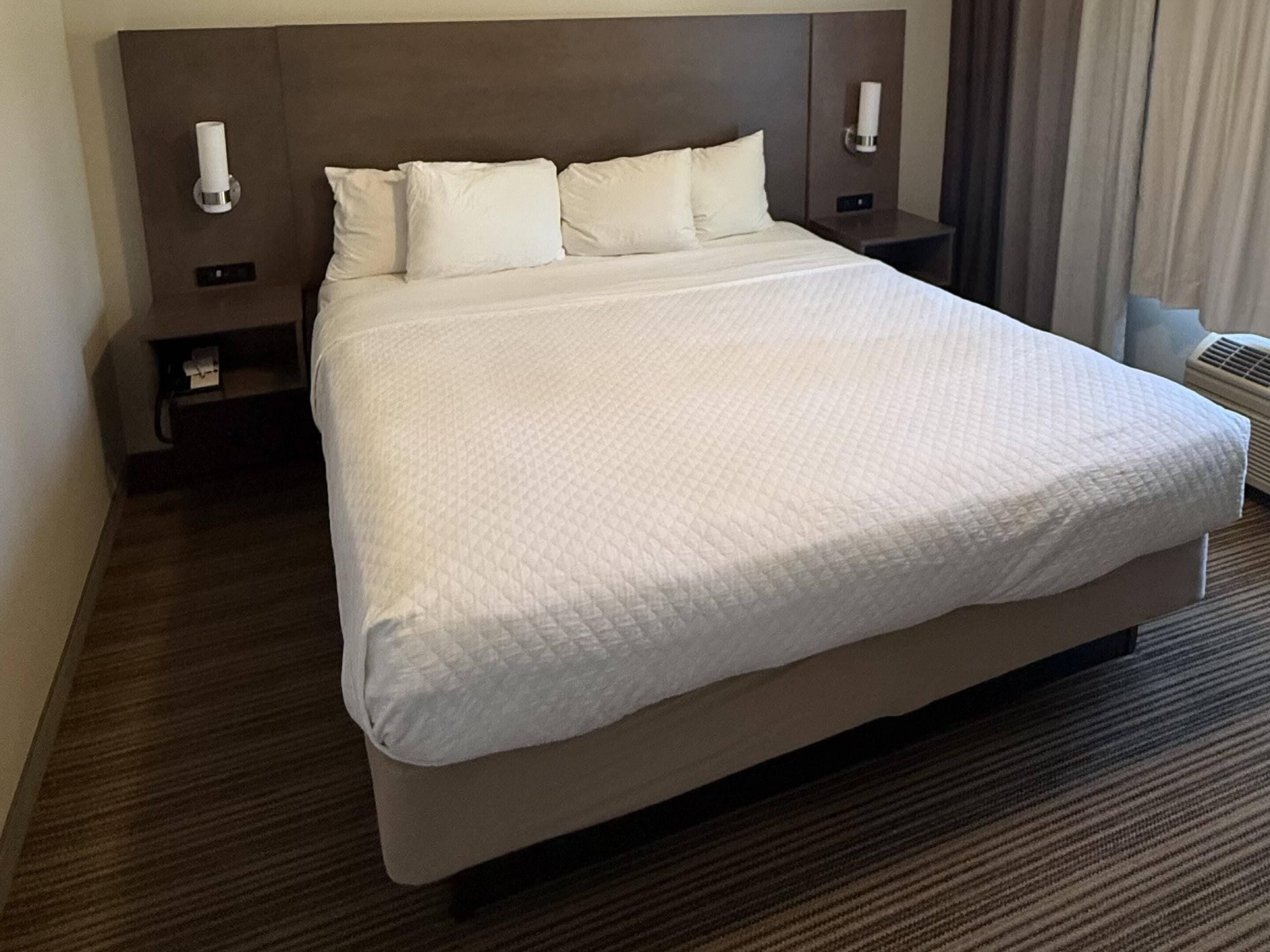 Une chambre d’hôtel avec un grand lit, deux tables de chevet et un climatiseur fixé au mur.