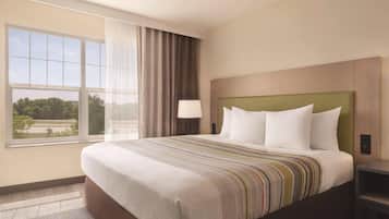 A hotel room with a large bed, a nightstand, a lamp, and a view of the outdoors through a window.